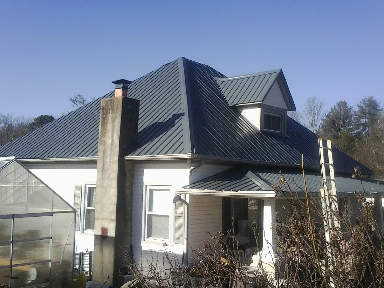 Dark blue standing seam metal roof on a white farmhouse with dormer — Slate & Tile Roof Repair by Roofing Brothers in Gibson