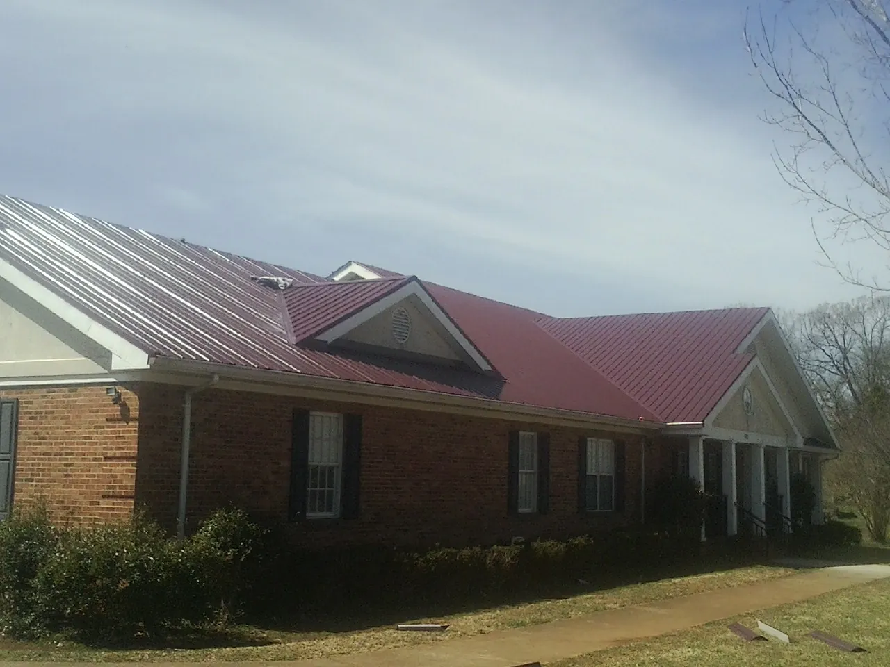 Red metal roof with gabled entries on a long brick building, from a Hail Damage Roof Repair job in Gibson